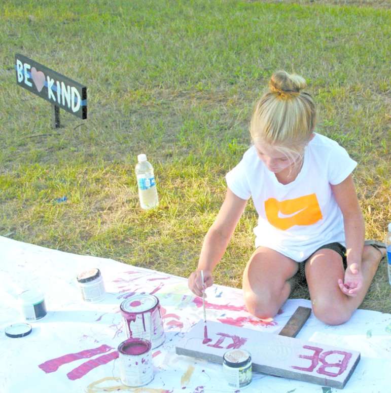 Ariana Nikolis, 9, paints BE KIND on a blank signboard. SPD Officer Justin Fuller’s friend, Tara Konieczny, had discovered Operation Kindness, so she prepared 250 signboards and brought them, along with brushes and paint, for anyone to paint the words and take them home to spread the good advice.
