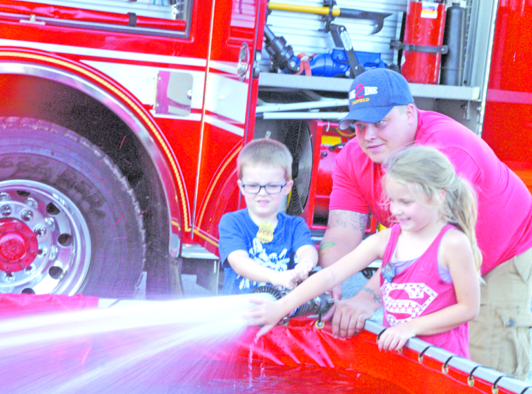 Maddy Agrafolo tests the strength of the water jet as Jack Doyle, 5, helps SFD Lieutenant Dan Godin hold the nozzle. They were spraying into a big reservoir tank set up next to the tanker fire engine.