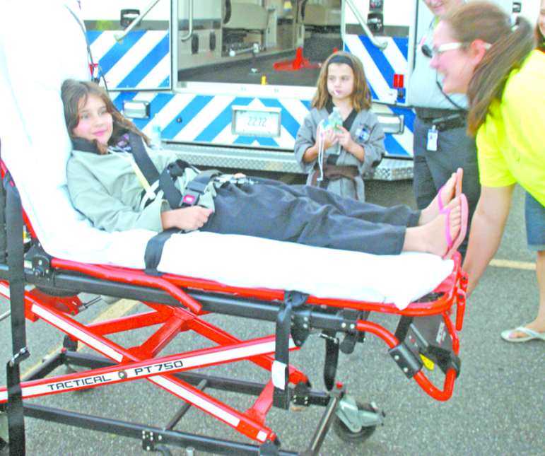 Sarah Michaelman, 10, helps her mother, Jen, demonstrate a guerney next to one of the SVAA’s ambulances, as her sister Katie, 8, watches. The girls were garbed for their practice at Integrity Martial Arts in Scitico.