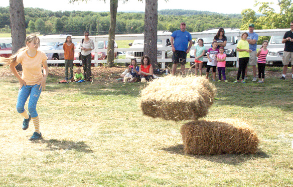Sarah McIntosh applies some body English to encourage her hay bale to tumble a bit further. As it turned out, she placed second to Sabdiel Rodriguez among the older girls hay bale toss competition.