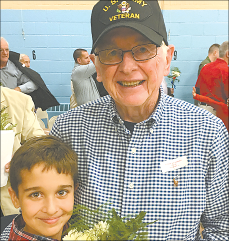 Second grader Joseph Zenczak smiles proudly next to his grandfather, veteran David Thayer, at the Spaulding School assembly on Veterans Day.