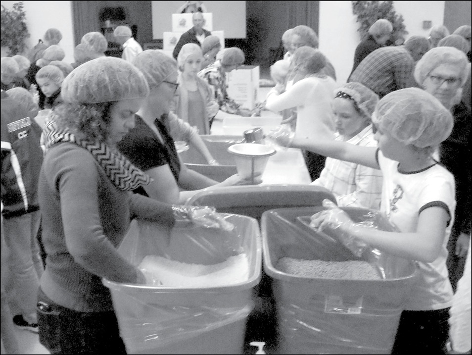 Volunteers fill bags of dehydrated soup at First Church on October 23. In the first station, counter-clockwise from right front: Katie Uzdarwin dumping lentils, Paige Remington about to add the salt, Abigail Schulz (only her arm showing) scooping vegetables, Mary McKenna waiting to remove the bag, and Kristen Uzdarwin scooping rice. At far right behind Katie, Ann Selvitelli returns with more bags.