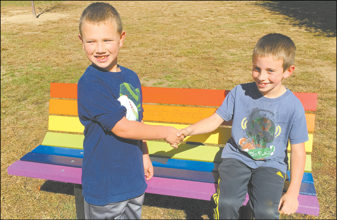 Spaulding School second grade students Jake Devanney and Ozzie Matejek shake at one of the new Buddy Benches on their playground.