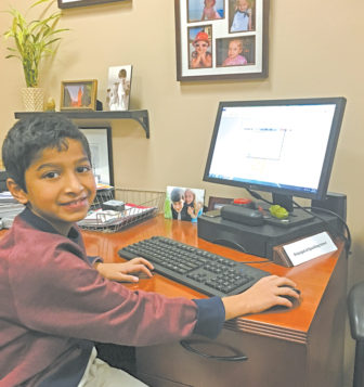 Second grade student Calvin Adappoor smiles for the camera at his desk as principal of Spaulding School.