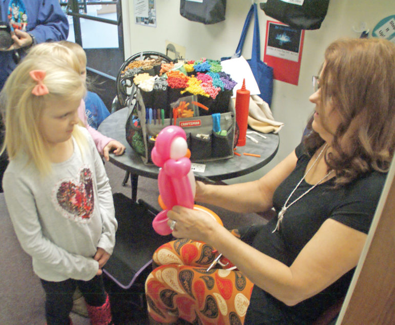 Deanna Savonin, 6, watches intently as balloon sculptor Cataline LaPointe ingeniously twists up a pink penguin for her.