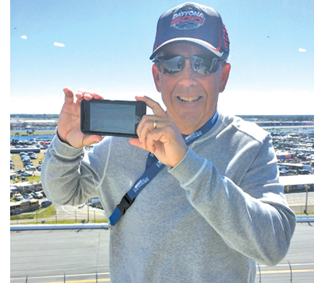 George Hermann is pictured reading the digital edition of the Observer at Turn 4 of the Daytona 500 on February 26, or so he says. How can we know he’s not checking lap times or interest rates?