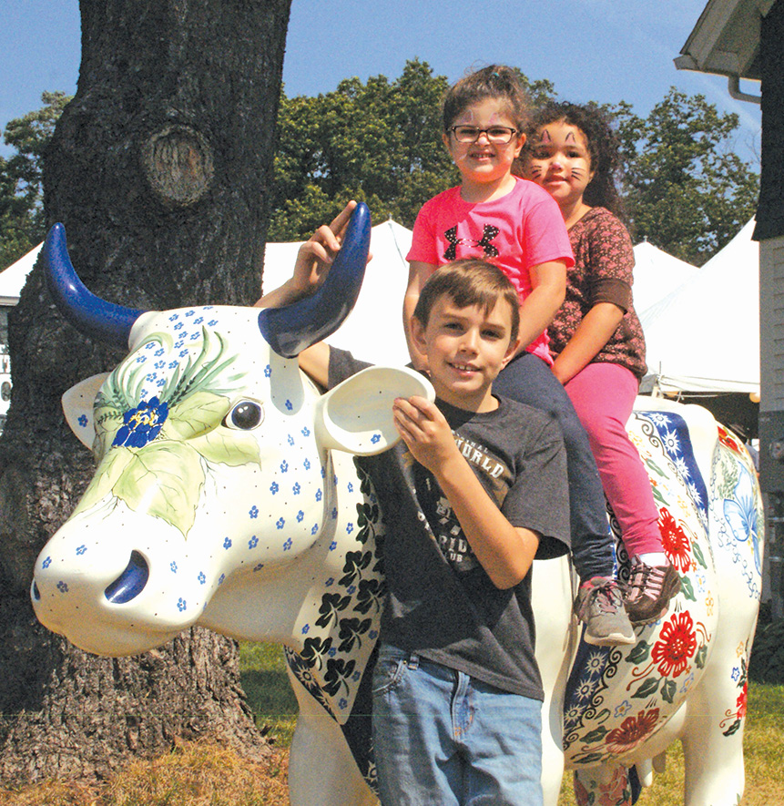 From front to back: Caleb York, 9; Sophia Piteo, 4; and Savannah York, 3; make friends with Hilltop Farm’s fancifully painted cow.
