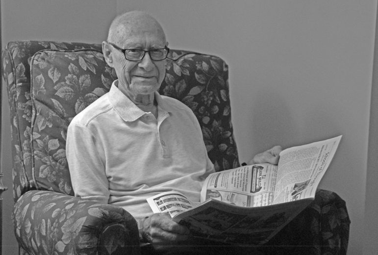 Comfortable in the library at Suffield on the River, nonagenarian Richard Hammerich looks up from reading The Suffield Observer.