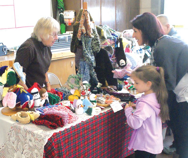 Jeannie Giauque tells Stephanie Garafolo and her daughter Giuliana how she knits the intricate specialties arrayed on her sales table at the Suffield Fire Department. The three-space garage had been emptied to make way for a wide variety of merchandise.