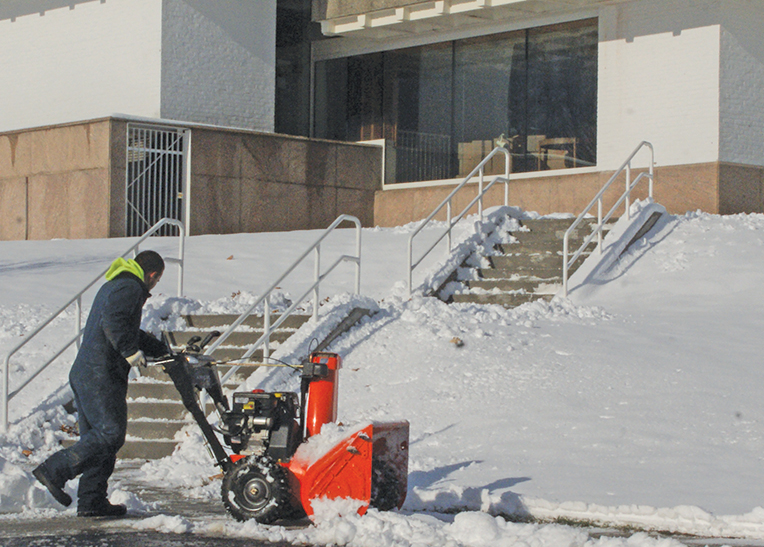 On Christmas Day, a snow removal contractor completes his task of clearing the morning snow from the sidewalks and the stairs of the Kent Memorial Library. Library patrons aren’t yet welcome, but work continues in the buildng, and the paths are occasionally used for a shortcut from the Main Street sidewalk to Bank Lane.