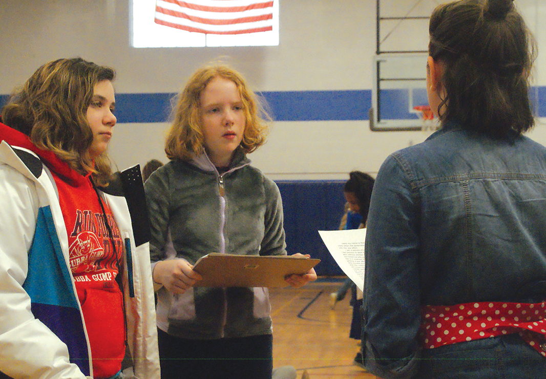 Members of the sixth grade White Team, Calli Pock and Bethany Richardson, left and center, interview Anika Gustafson of the Blue Team, who portrayed Rosie the Riveter, a symbolic character from the Second World War.